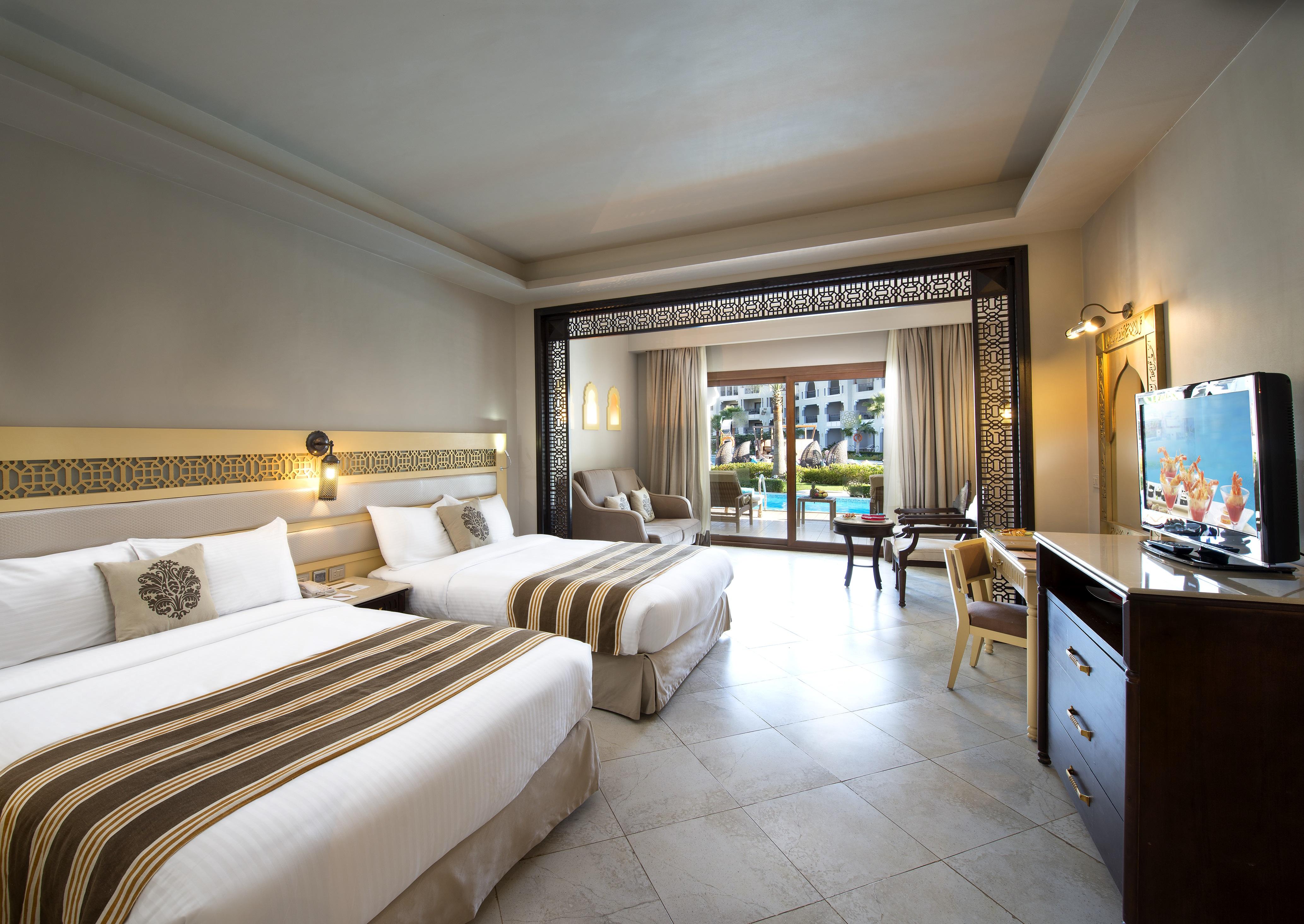 Sunrise Arabian Beach Resort Sharm El-Sheikh Exterior foto The photo shows a well-decorated hotel room. It features two beds with white linens and decorative brown striped accents. There is a large window with sheer curtains that provides a view of the outdoors, suggesting a pool area or gardens. The room in
