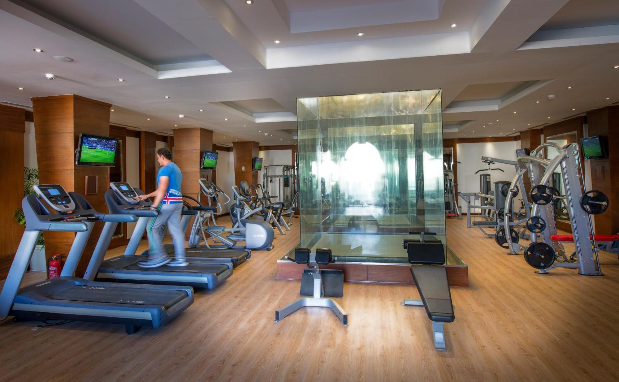 Sunrise Arabian Beach Resort Sharm El-Sheikh Exterior foto The photo shows a modern gym with various exercise equipment. On the left side, there are treadmills, with a person walking on one of them. In the center, there's a glass-walled space, which likely serves as a private area for workouts or classes. Th